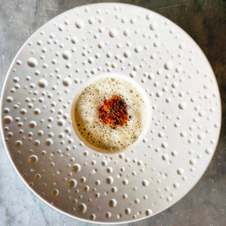A pale emulsion dotted like a seed head, on a white plate